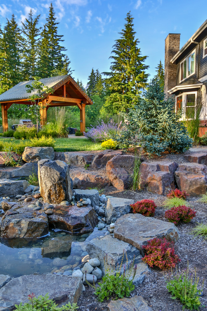 This is an example of a large arts and crafts backyard patio in Seattle with a water feature, natural stone pavers and a gazebo/cabana.