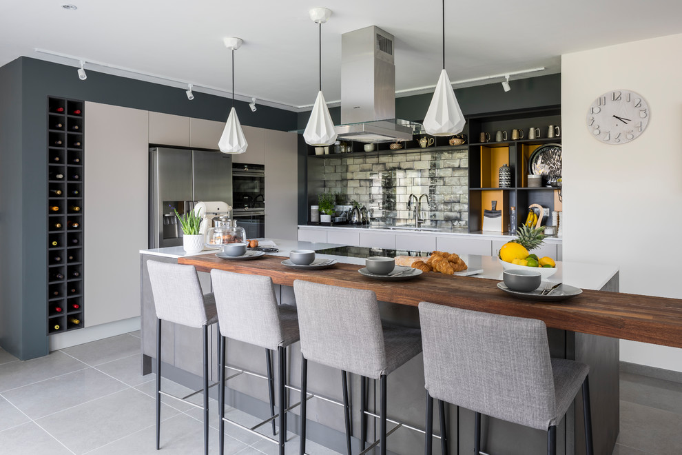 Photo of a mid-sized contemporary l-shaped open plan kitchen in Other with a drop-in sink, flat-panel cabinets, solid surface benchtops, mirror splashback, stainless steel appliances, ceramic floors, grey floor, grey cabinets and a peninsula.