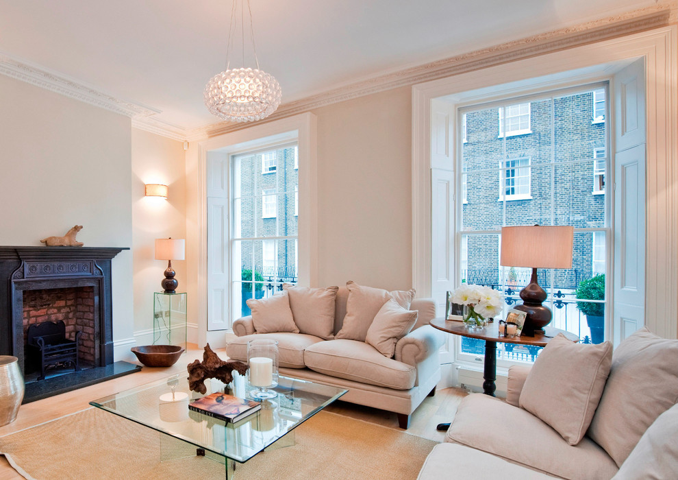 This is an example of a transitional formal living room in London with beige walls, medium hardwood floors, a standard fireplace and no tv.