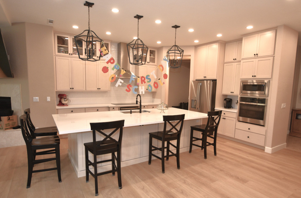 Kitchen - large transitional l-shaped vinyl floor and beige floor kitchen idea with an undermount sink, shaker cabinets, light wood cabinets, solid surface countertops, white backsplash, porcelain backsplash, stainless steel appliances, an island and white countertops
