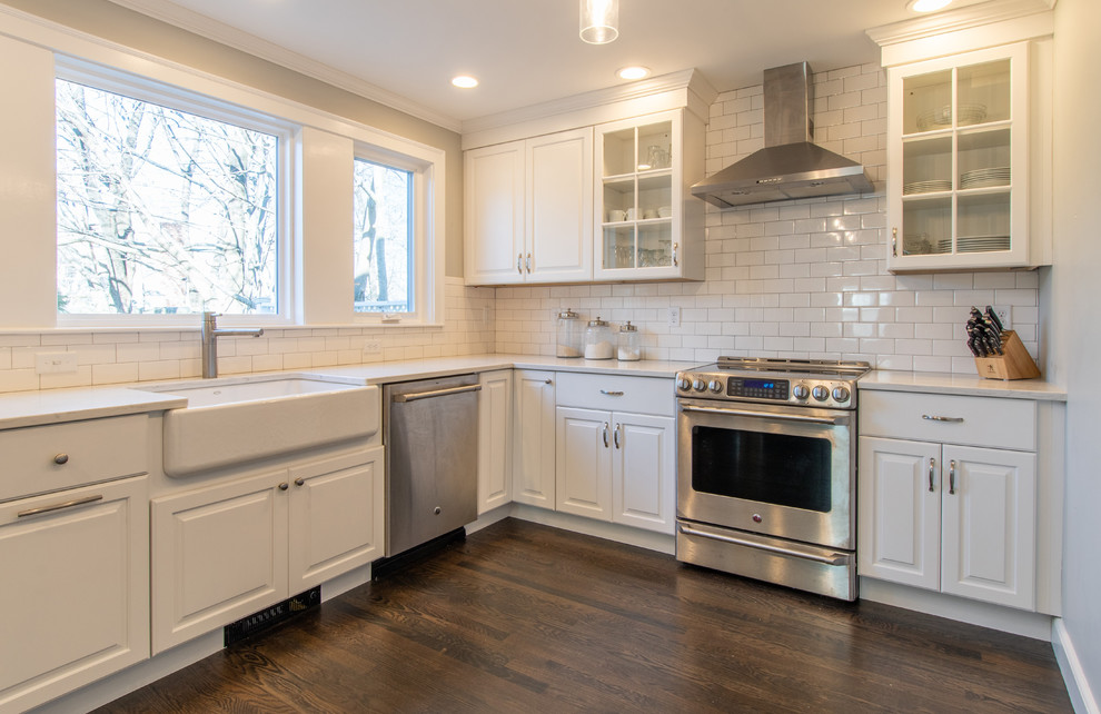 Photo of a large country l-shaped eat-in kitchen in Boston with a farmhouse sink, raised-panel cabinets, yellow cabinets, quartz benchtops, white splashback, subway tile splashback, stainless steel appliances, dark hardwood floors, no island, brown floor and white benchtop.