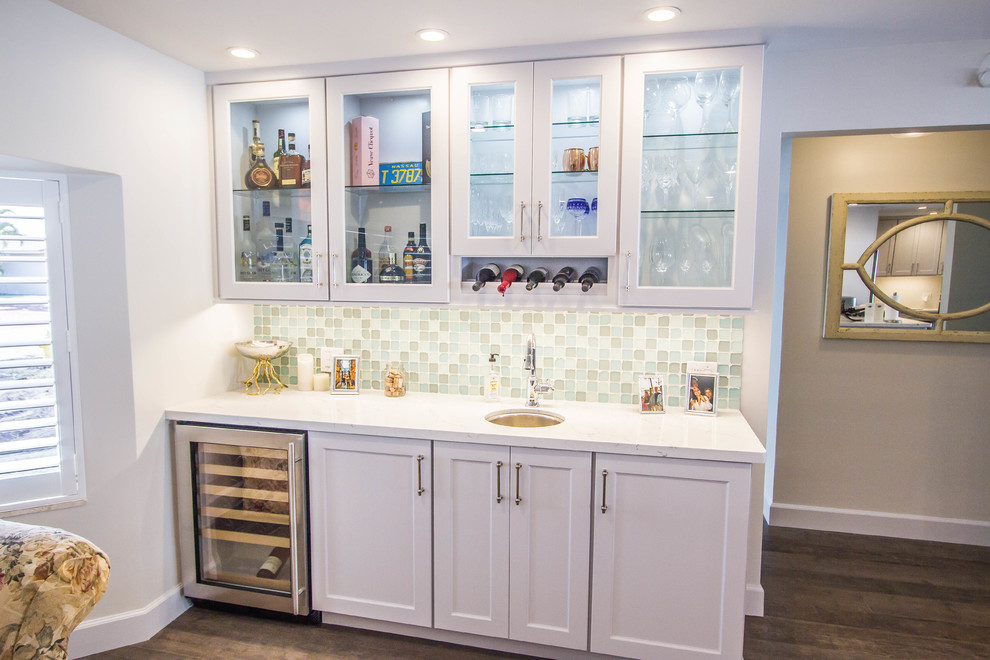 Mid-sized beach style single-wall wet bar in Miami with an undermount sink, shaker cabinets, white cabinets, quartzite benchtops, multi-coloured splashback, glass tile splashback, dark hardwood floors, brown floor and white benchtop.