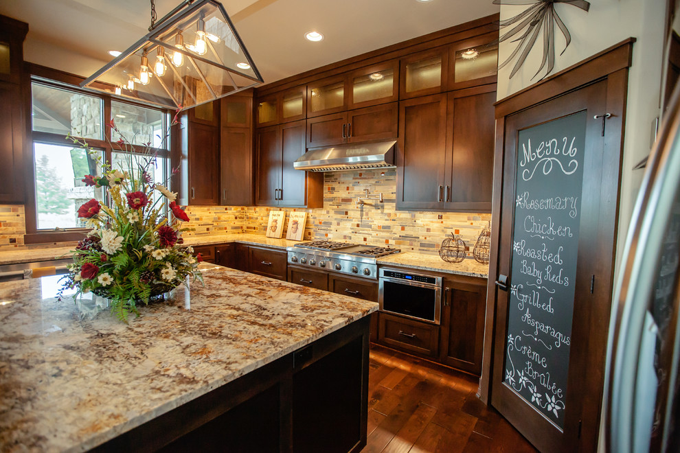 This is an example of a large transitional u-shaped eat-in kitchen in Milwaukee with a farmhouse sink, shaker cabinets, dark wood cabinets, granite benchtops, multi-coloured splashback, stainless steel appliances, dark hardwood floors and with island.