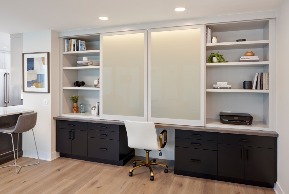 Inspiration for a small contemporary study room in Chicago with white walls, light hardwood floors, a built-in desk and brown floor.