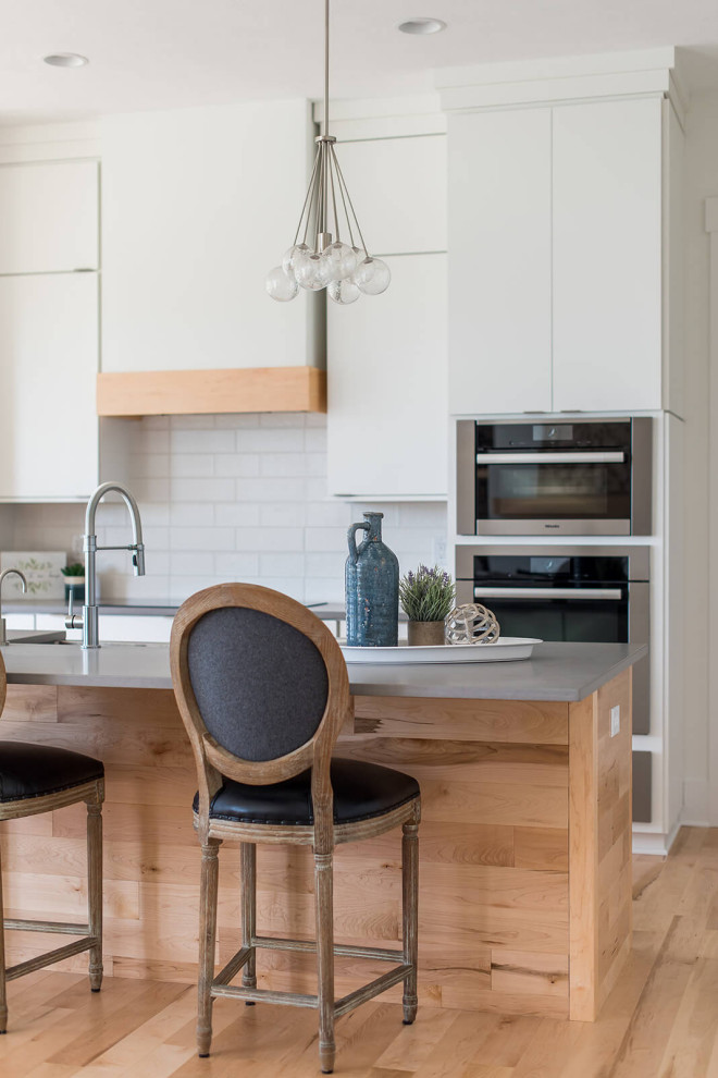Inredning av ett minimalistiskt mellanstort kök, med en undermonterad diskho, släta luckor, vita skåp, rostfria vitvaror, mellanmörkt trägolv och en köksö