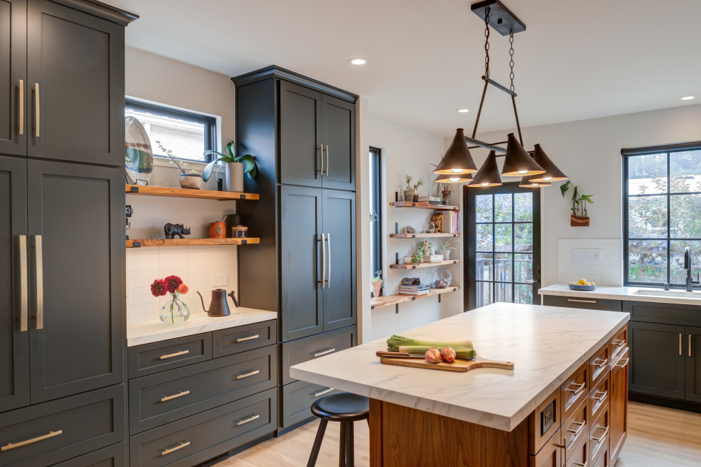 Inspiration for a large transitional l-shaped eat-in kitchen in San Francisco with an undermount sink, shaker cabinets, green cabinets, quartz benchtops, white splashback, ceramic splashback, black appliances, light hardwood floors, with island and white benchtop.