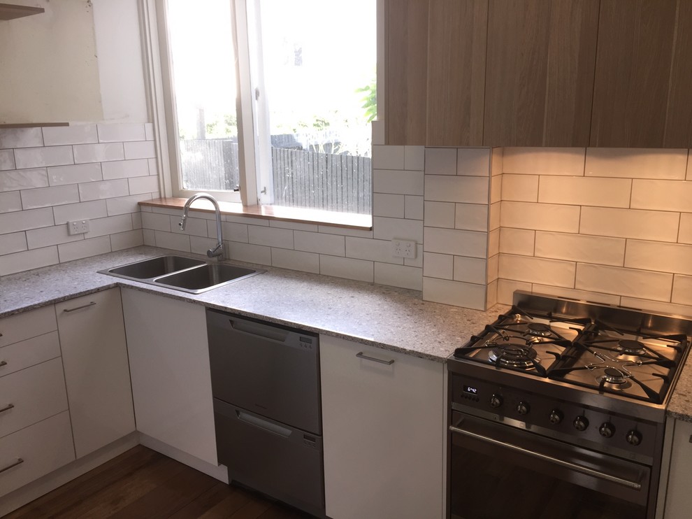 Small contemporary u-shaped separate kitchen in Melbourne with a double-bowl sink, flat-panel cabinets, white cabinets, granite benchtops, white splashback, stainless steel appliances, medium hardwood floors, ceramic splashback and grey benchtop.