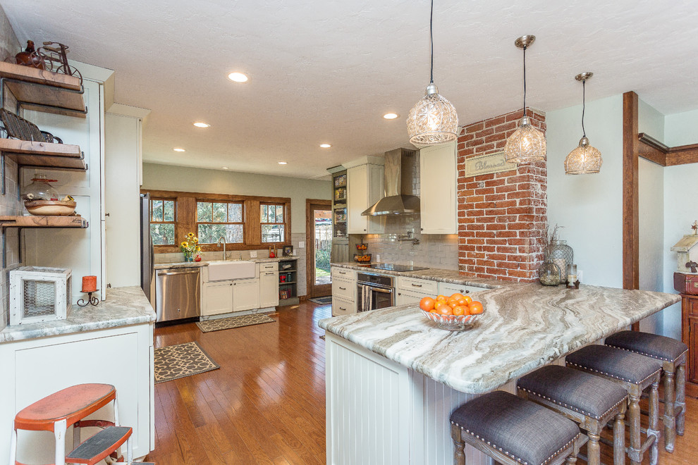Inspiration for a large transitional l-shaped medium tone wood floor and brown floor open concept kitchen remodel in Phoenix with a farmhouse sink, shaker cabinets, white cabinets, quartzite countertops, gray backsplash, porcelain backsplash, stainless steel appliances and no island
