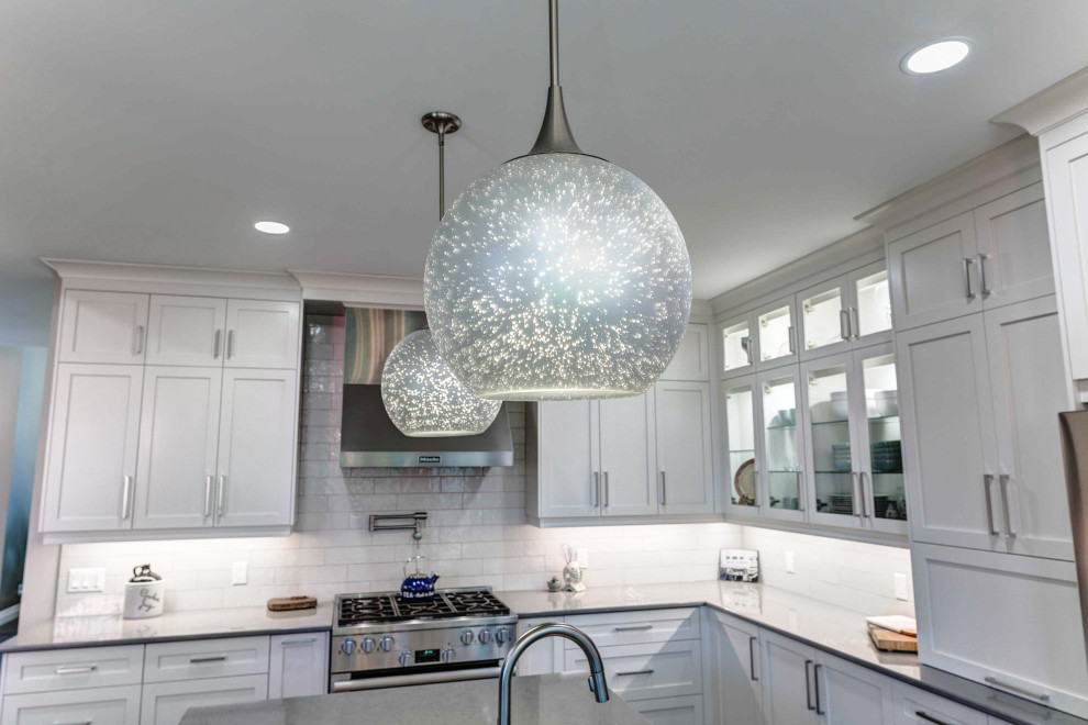 Transitional l-shaped eat-in kitchen photo with a farmhouse sink, shaker cabinets, white cabinets, quartz countertops, porcelain backsplash, stainless steel appliances, an island and white countertops