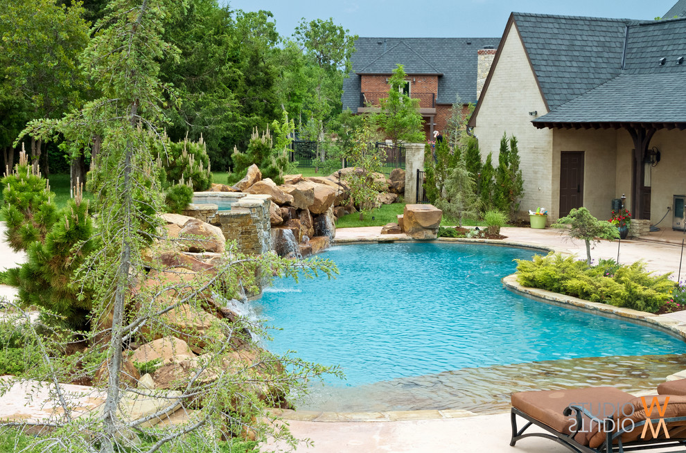 Inspiration for a mid-sized traditional backyard kidney-shaped lap pool in Oklahoma City with a water feature and natural stone pavers.