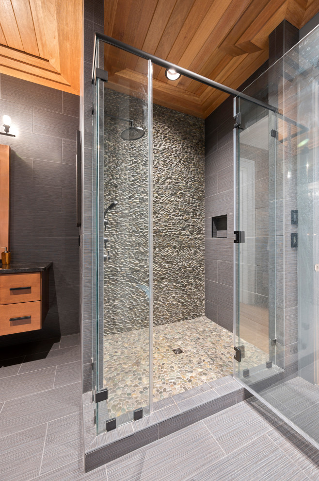 This is an example of a large beach style master bathroom in Other with furniture-like cabinets, light wood cabinets, gray tile, porcelain tile, grey walls, pebble tile floors, an undermount sink, granite benchtops, grey floor, a hinged shower door, black benchtops, a single vanity, a built-in vanity and wood.
