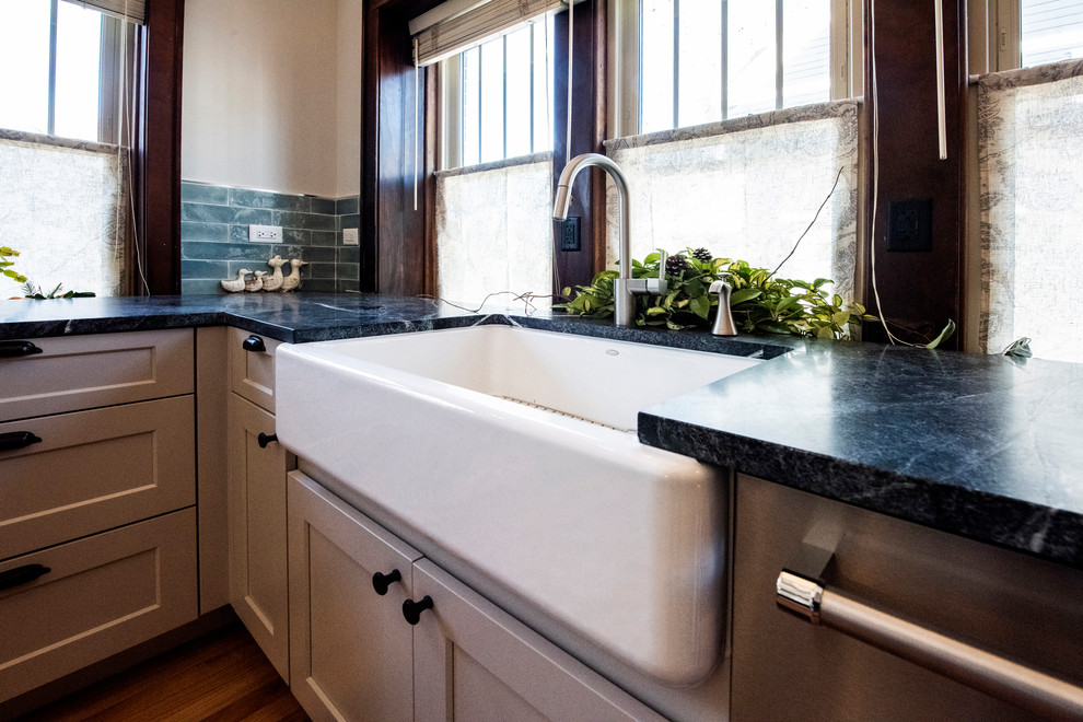 This is an example of a small arts and crafts u-shaped eat-in kitchen in Chicago with a farmhouse sink, shaker cabinets, grey cabinets, granite benchtops, blue splashback, glass tile splashback, stainless steel appliances, medium hardwood floors, no island, brown floor and green benchtop.