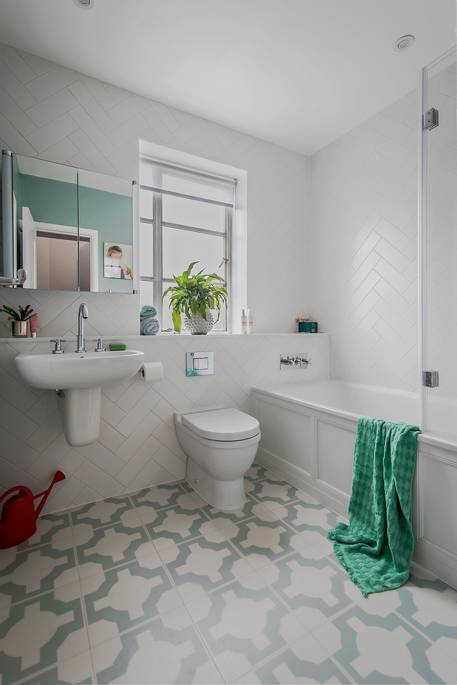 This is an example of a mid-sized transitional kids bathroom in Hampshire with a drop-in tub, a shower/bathtub combo, a one-piece toilet, white tile, ceramic tile, vinyl floors, a wall-mount sink and green floor.