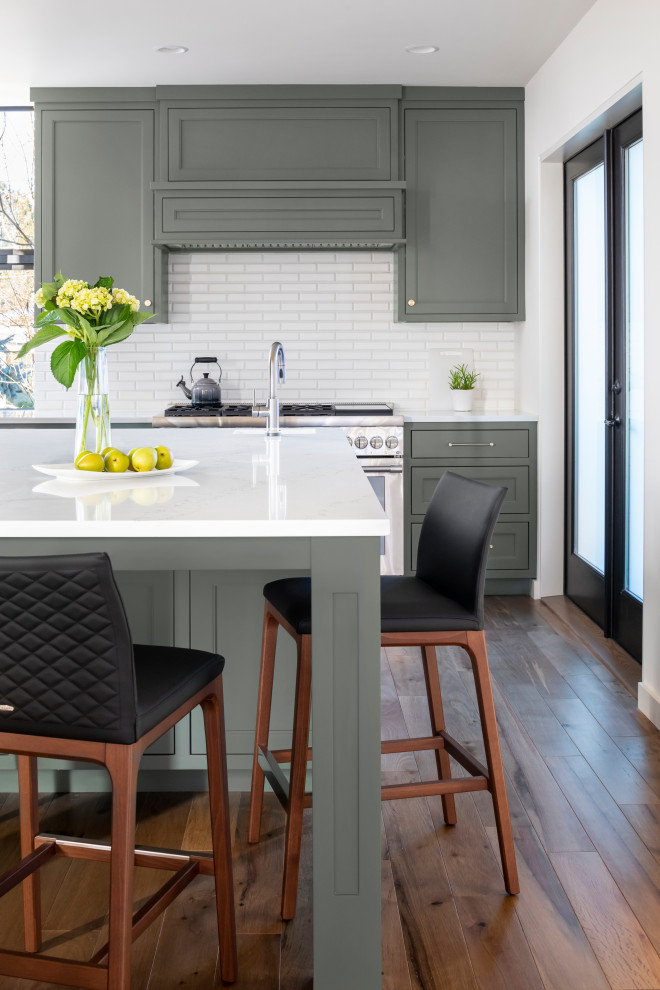 Photo of a medium sized contemporary l-shaped kitchen/diner in Seattle with a submerged sink, beaded cabinets, green cabinets, engineered stone countertops, yellow splashback, metro tiled splashback, stainless steel appliances, medium hardwood flooring, an island and white worktops.