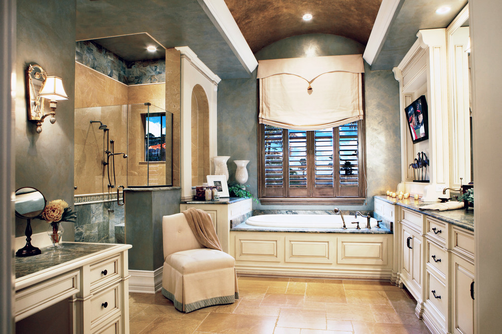 Photo of a mid-sized mediterranean master bathroom in Miami with recessed-panel cabinets, white cabinets, a drop-in tub, an alcove shower, beige tile, blue tile, blue walls, beige floor, a hinged shower door, a two-piece toilet, stone tile, limestone floors, an undermount sink and granite benchtops.