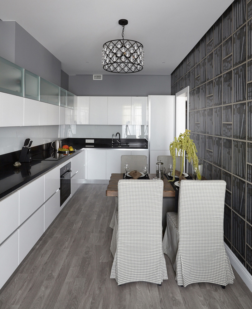 Inspiration for a mid-sized contemporary l-shaped eat-in kitchen in Moscow with flat-panel cabinets, white cabinets, quartz benchtops, white splashback, glass sheet splashback, black appliances, no island, black benchtop and grey floor.