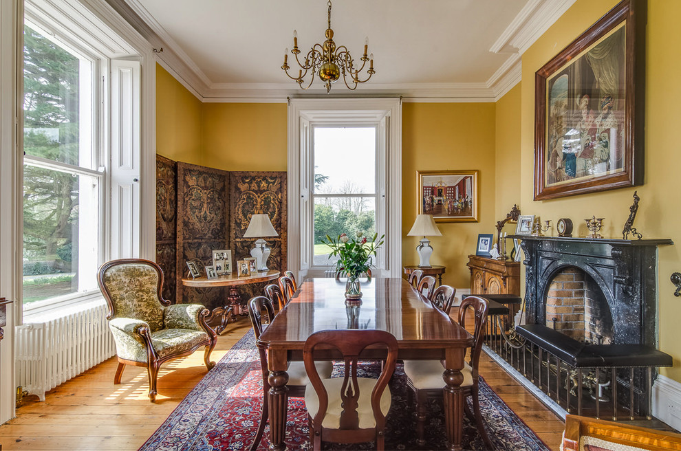 Photo of a large traditional separate dining room in Belfast with yellow walls, light hardwood floors and a standard fireplace.