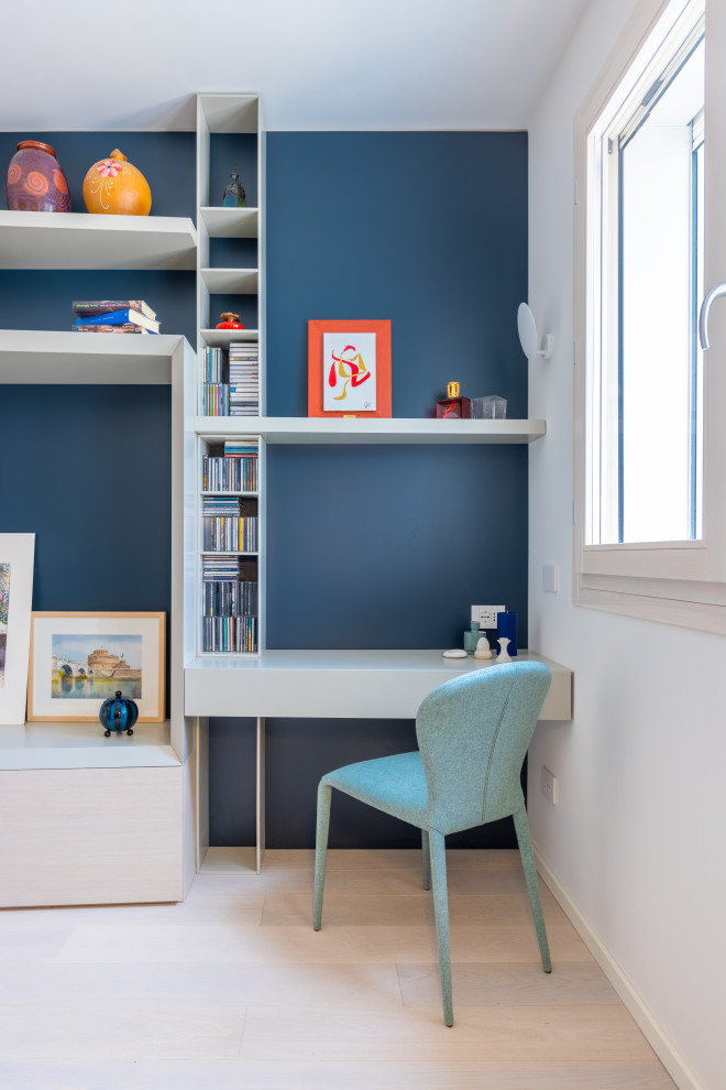 Imagen de estudio minimalista de tamaño medio con paredes azules, suelo de madera clara, escritorio empotrado y suelo beige