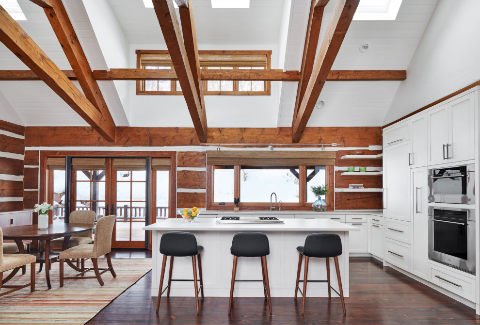 Inspiration for a country l-shaped eat-in kitchen in Denver with stainless steel appliances, shaker cabinets, white cabinets, timber splashback, dark hardwood floors, with island, white benchtop, exposed beam, timber and vaulted.