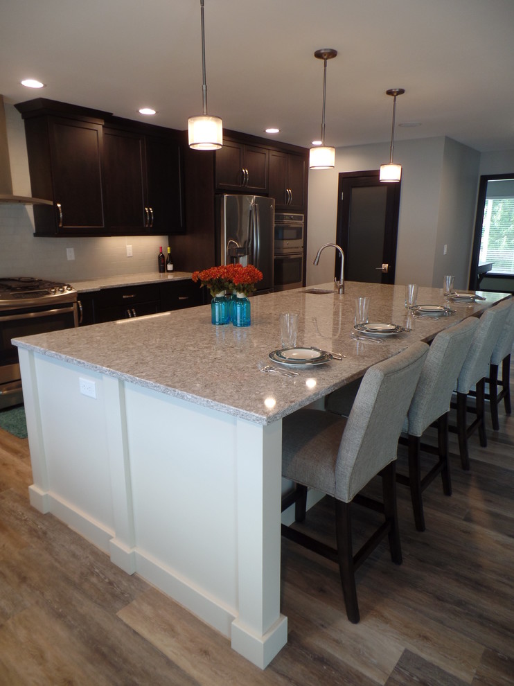 Inspiration for a large transitional l-shaped medium tone wood floor and beige floor eat-in kitchen remodel in Cedar Rapids with an undermount sink, shaker cabinets, dark wood cabinets, granite countertops, white backsplash, subway tile backsplash, stainless steel appliances and an island