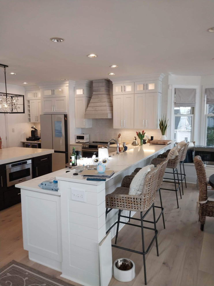 Transitional l-shaped medium tone wood floor and brown floor open concept kitchen photo in DC Metro with an undermount sink, shaker cabinets, white cabinets, quartz countertops, white backsplash, subway tile backsplash, stainless steel appliances, two islands and white countertops