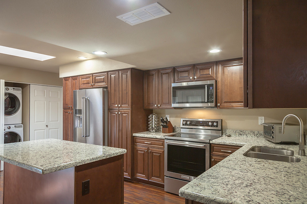 Mid-sized transitional l-shaped laminate floor and brown floor enclosed kitchen photo in Phoenix with an undermount sink, shaker cabinets, medium tone wood cabinets, granite countertops, multicolored backsplash, stone slab backsplash, stainless steel appliances and an island