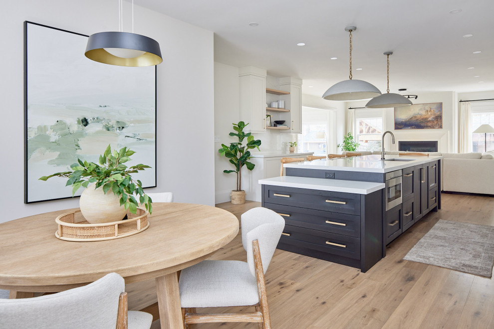 Mid-sized transitional medium tone wood floor and brown floor kitchen/dining room combo photo with white walls, a standard fireplace and a stone fireplace