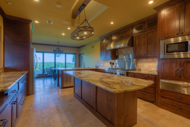 Example of a large transitional u-shaped travertine floor eat-in kitchen design in Austin with shaker cabinets, medium tone wood cabinets, granite countertops, beige backsplash, stone tile backsplash, stainless steel appliances and an island