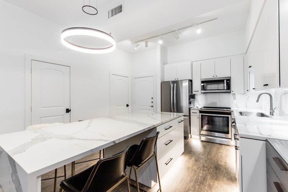 Small modern l-shaped open plan kitchen in Dallas with flat-panel cabinets, white cabinets, white splashback, stainless steel appliances, vinyl floors, with island, brown floor, white benchtop, an undermount sink, glass benchtops and porcelain splashback.