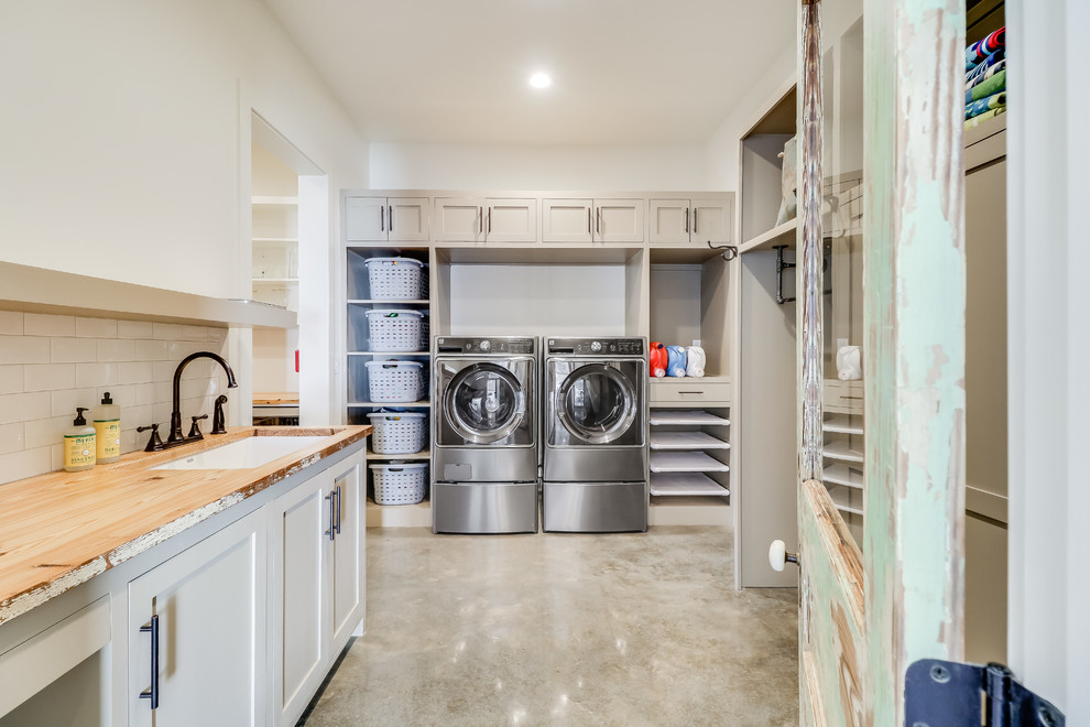 This is an example of a country u-shaped utility room in Jackson with an undermount sink, shaker cabinets, beige cabinets, wood benchtops, white walls, concrete floors, a side-by-side washer and dryer, grey floor and beige benchtop.