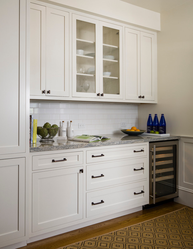 Photo of a mid-sized traditional single-wall wet bar in San Francisco with shaker cabinets, white cabinets, granite benchtops, white splashback, subway tile splashback, medium hardwood floors, no sink, brown floor and grey benchtop.