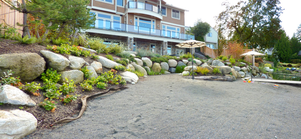 This is an example of a mid-sized beach style backyard partial sun garden in Seattle with natural stone pavers and a retaining wall.