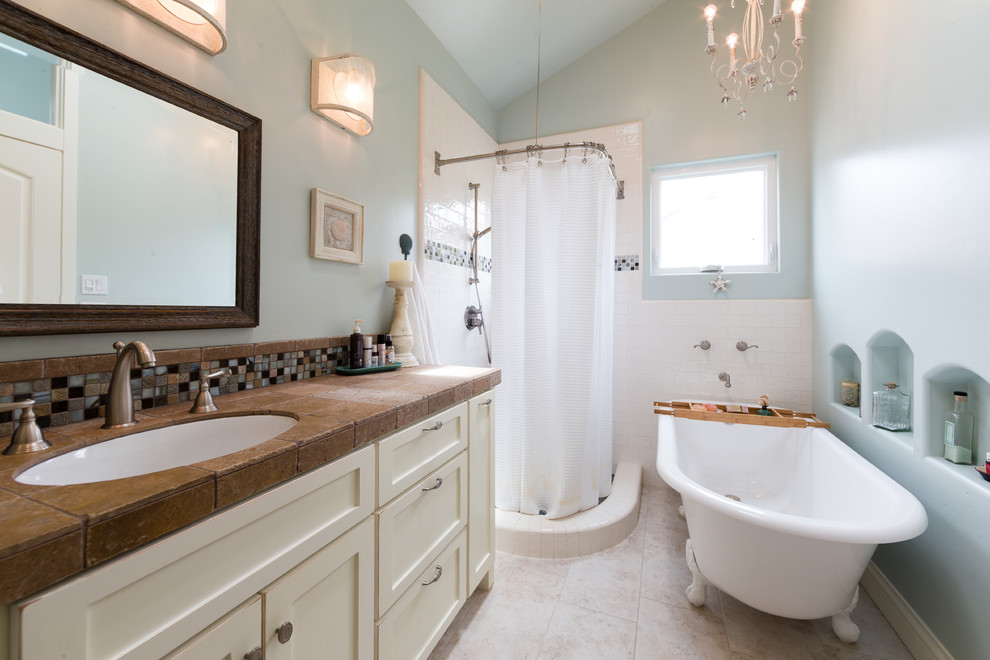 Photo of a beach style 3/4 bathroom in San Luis Obispo with shaker cabinets, white cabinets, a claw-foot tub, a corner shower, white tile, subway tile, blue walls, an undermount sink, tile benchtops, beige floor, a shower curtain and brown benchtops.