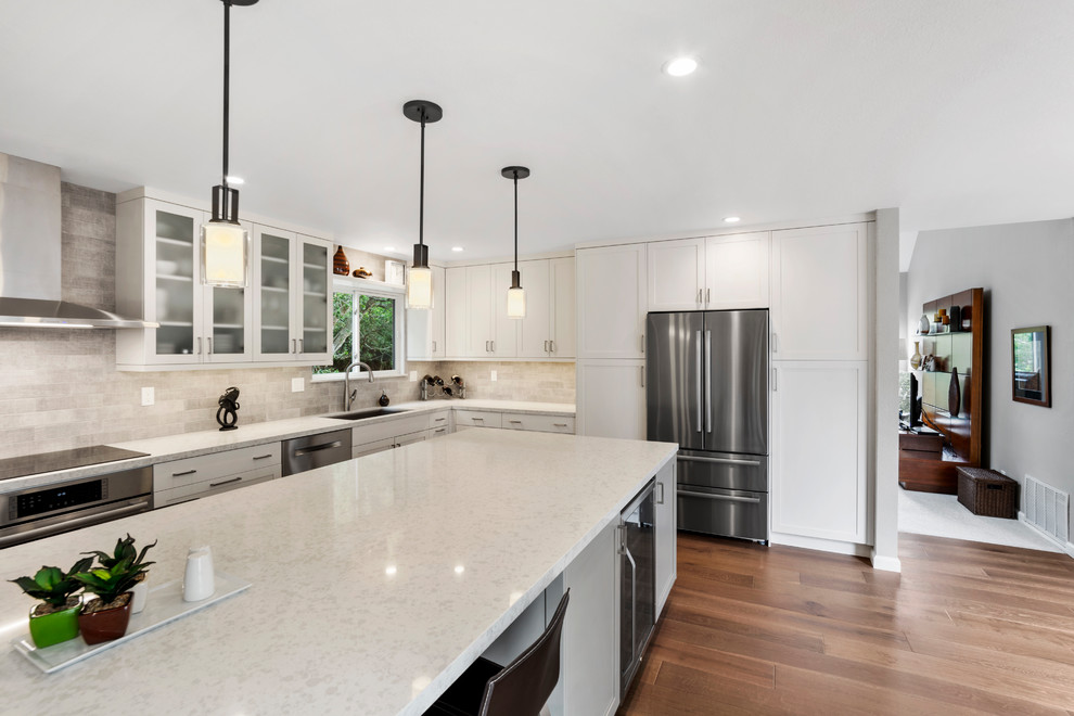 Example of a mid-sized transitional l-shaped medium tone wood floor and brown floor kitchen pantry design with an undermount sink, shaker cabinets, white cabinets, quartz countertops, beige backsplash, subway tile backsplash, stainless steel appliances, an island and beige countertops