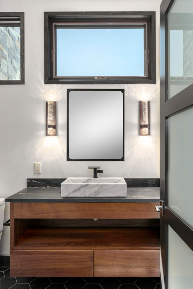 This is an example of a mid-sized contemporary 3/4 bathroom in Baltimore with recessed-panel cabinets, medium wood cabinets, an open shower, a one-piece toilet, black tile, ceramic tile, white walls, porcelain floors, a vessel sink, soapstone benchtops, black floor, a hinged shower door, black benchtops, a shower seat, a single vanity and a floating vanity.