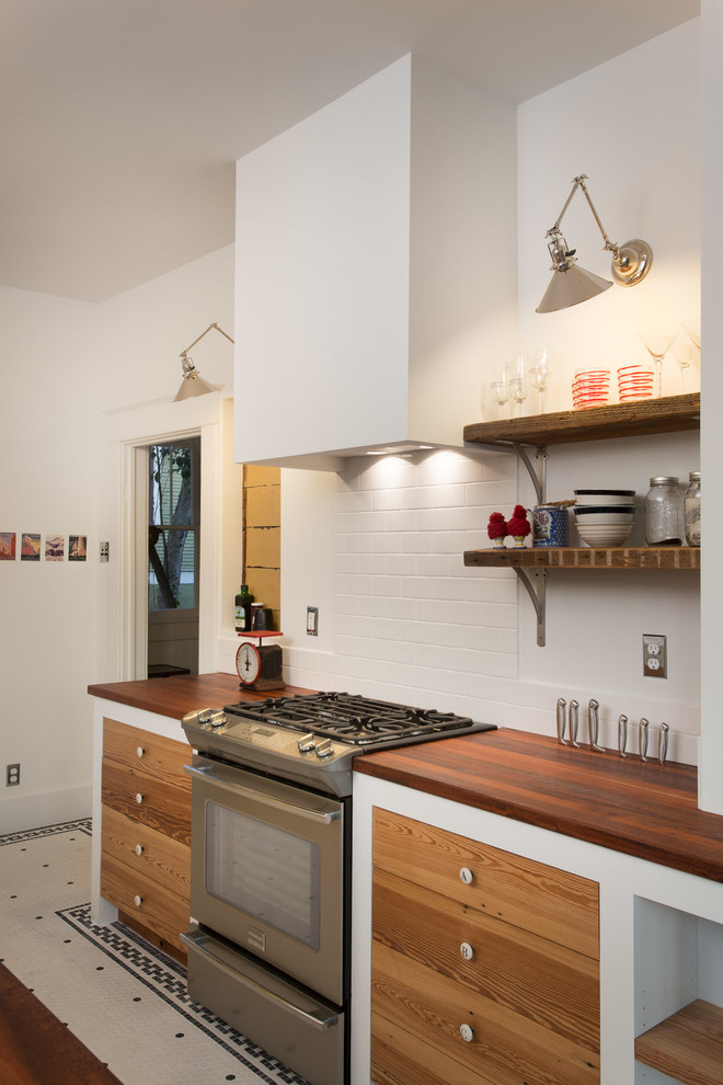Mid-sized eclectic l-shaped kitchen in Austin with a double-bowl sink, flat-panel cabinets, medium wood cabinets, wood benchtops, white splashback, stainless steel appliances, ceramic floors and subway tile splashback.