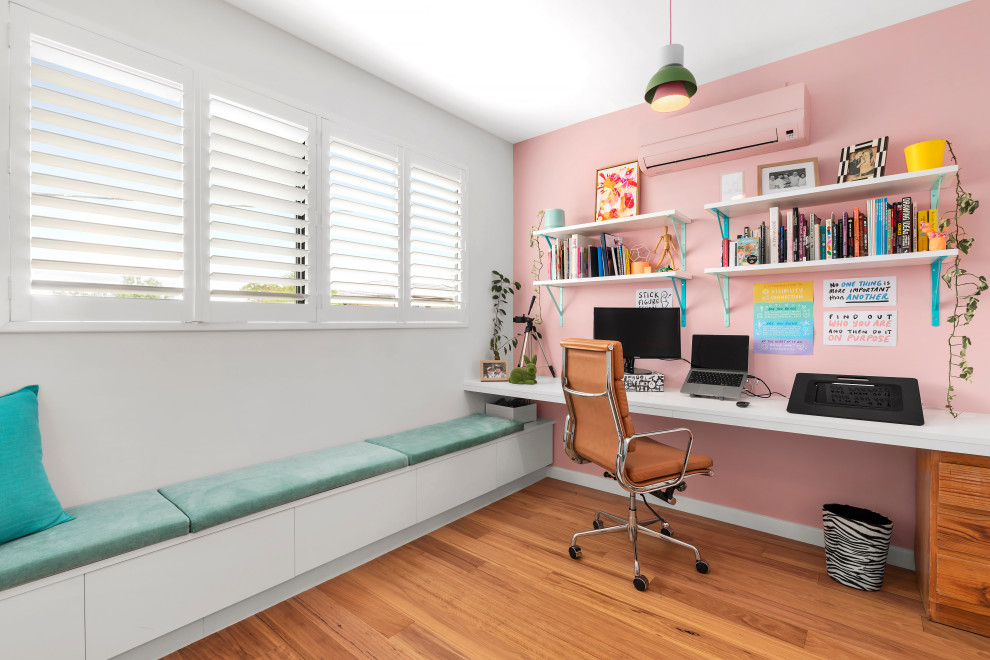 Modern home office in Melbourne with pink walls, light hardwood flooring and a built-in desk.