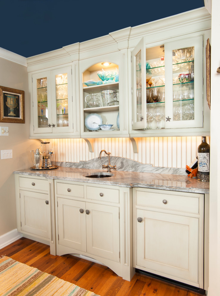 Photo of a mid-sized traditional single-wall wet bar in New York with an undermount sink, glass-front cabinets, beige cabinets, marble benchtops, grey splashback, stone slab splashback, medium hardwood floors and brown floor.
