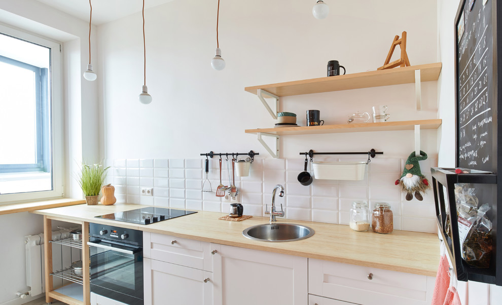 Photo of a small scandinavian single-wall separate kitchen in Moscow with a drop-in sink, white cabinets, white splashback, subway tile splashback, black appliances, no island and raised-panel cabinets.