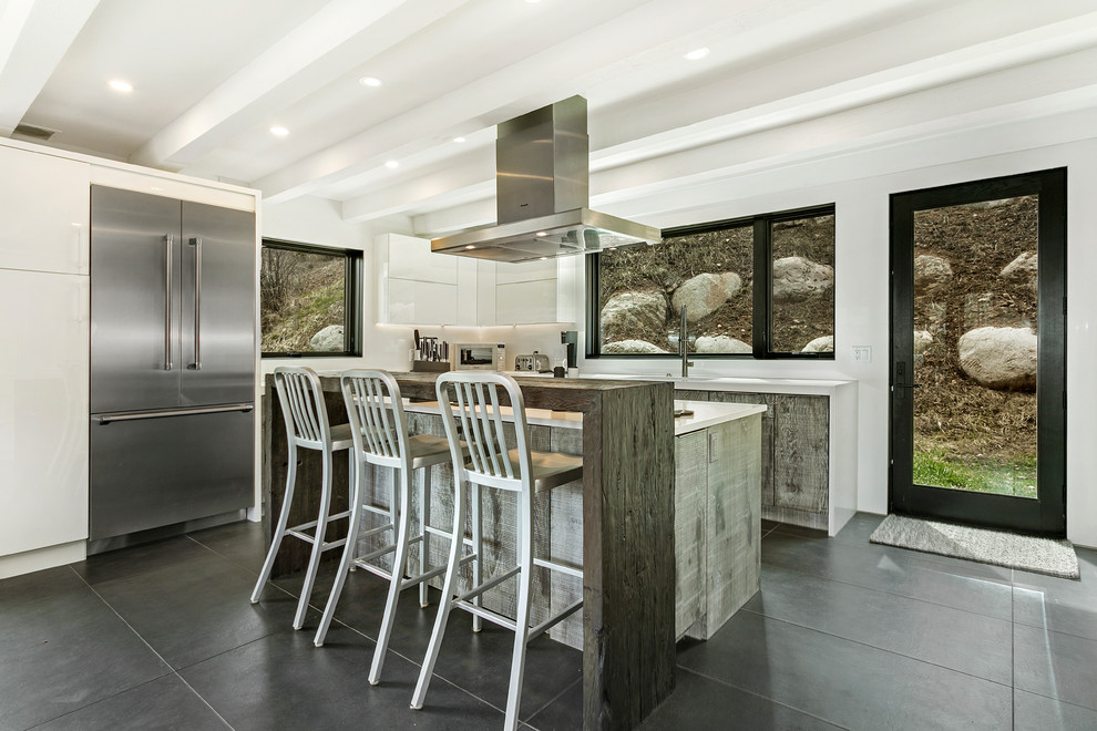 Photo of a mid-sized contemporary l-shaped eat-in kitchen in Denver with an undermount sink, flat-panel cabinets, distressed cabinets, quartz benchtops, white splashback, stone slab splashback, stainless steel appliances, porcelain floors, with island, grey floor and white benchtop.