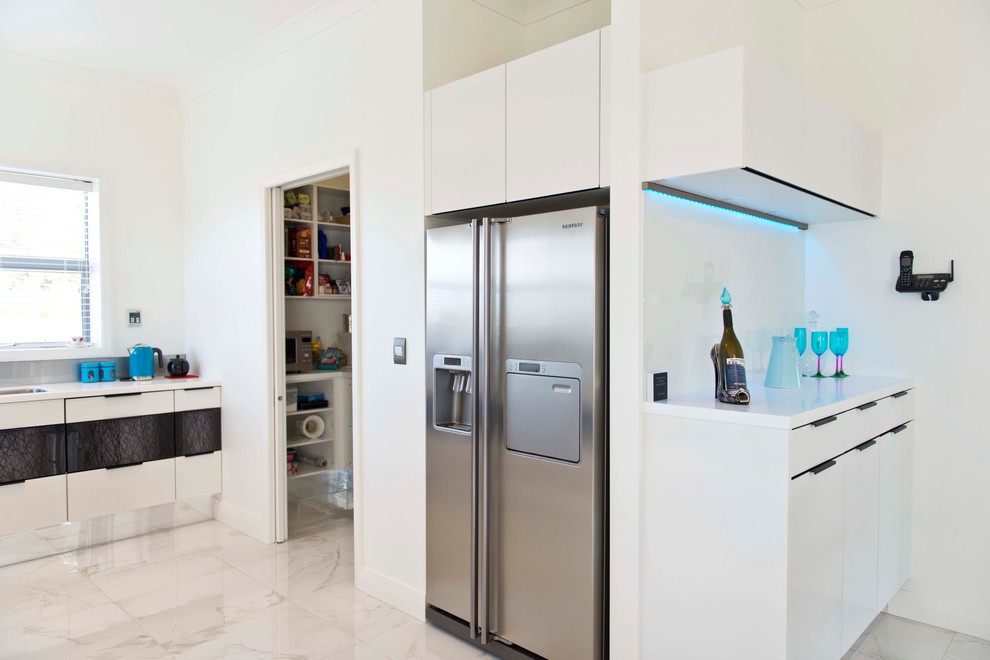 This is an example of a large modern l-shaped kitchen pantry in Christchurch with an undermount sink, flat-panel cabinets, white cabinets, solid surface benchtops, yellow splashback, glass sheet splashback, stainless steel appliances, ceramic floors, multiple islands and white floor.