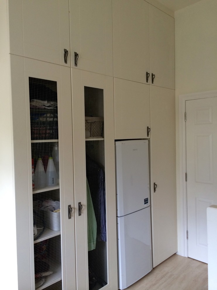Photo of a contemporary single-wall utility room with shaker cabinets, beige cabinets and light hardwood flooring.