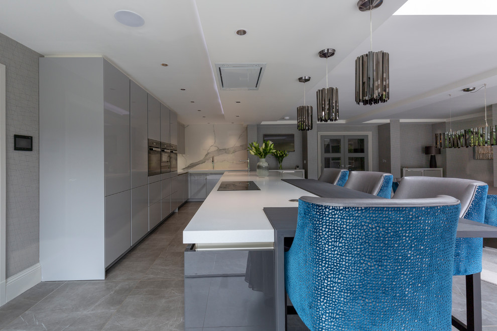 Large contemporary l-shaped open plan kitchen in Cheshire with flat-panel cabinets, grey cabinets, white splashback, marble splashback, black appliances, porcelain floors, with island, grey floor and white benchtop.