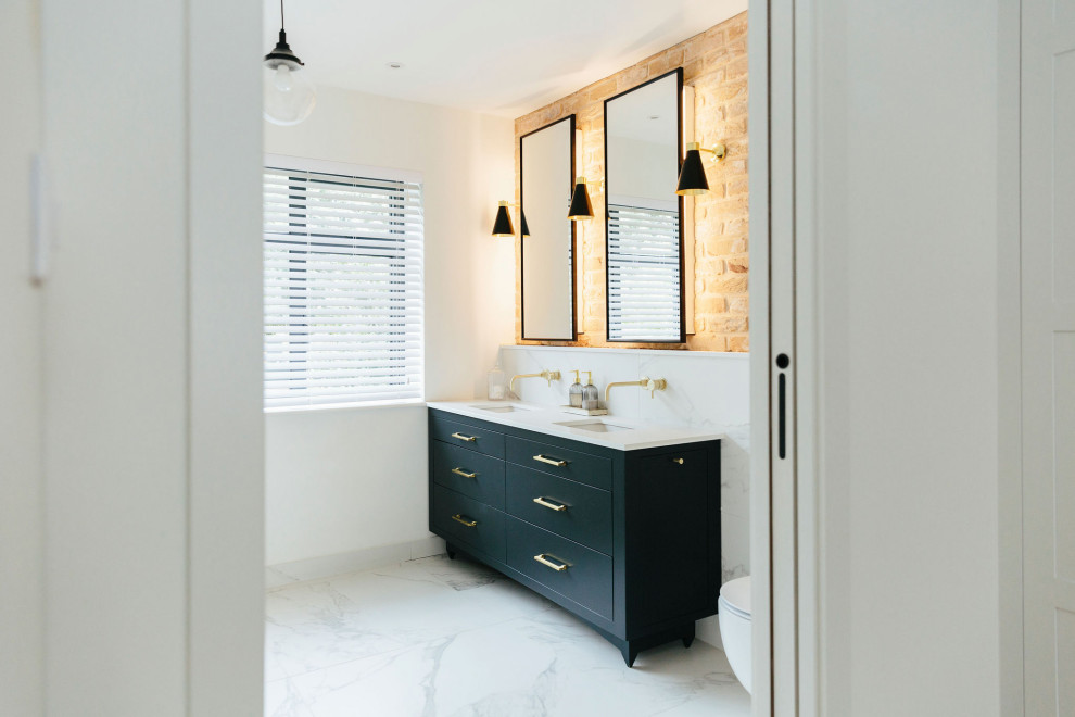 Inspiration for a large transitional master bathroom in London with flat-panel cabinets, blue cabinets, an open shower, a wall-mount toilet, white tile, marble, white walls, marble floors, a drop-in sink, marble benchtops, white floor, an open shower, white benchtops, a double vanity, a built-in vanity and brick walls.