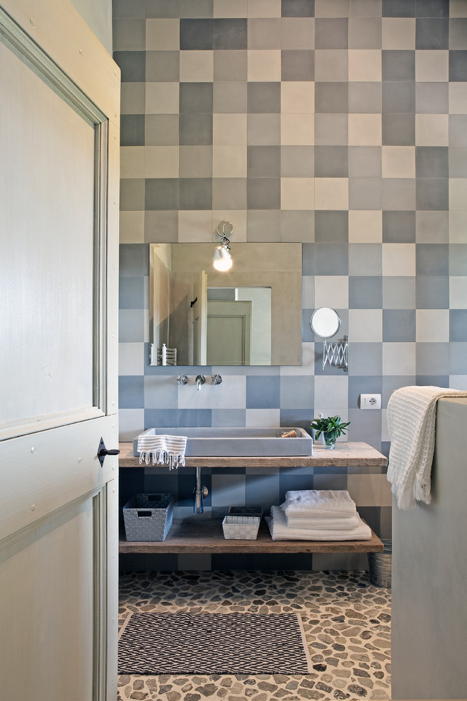 This is an example of a small mediterranean bathroom in New York with multi-coloured tile, pebble tile floors, a vessel sink, blue walls, marble benchtops and multi-coloured floor.