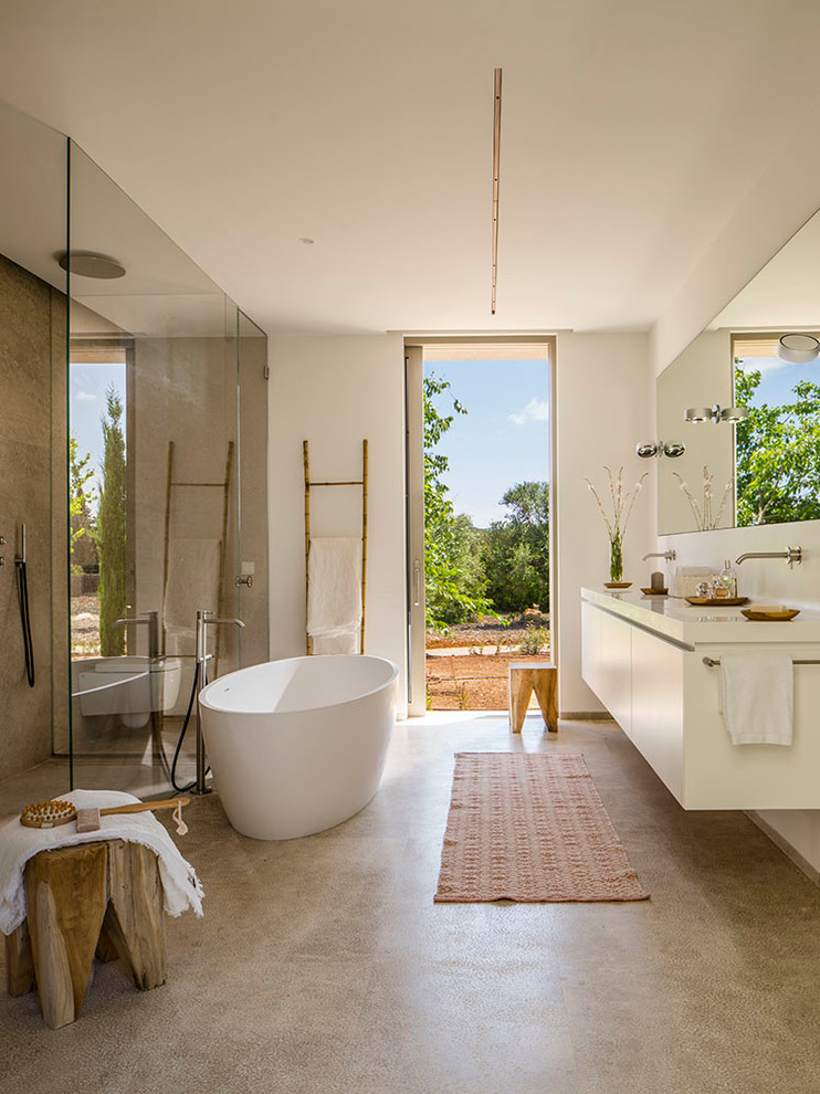 Inspiration for a large mediterranean master bathroom in Other with flat-panel cabinets, white cabinets, a freestanding tub, a curbless shower, white walls, concrete floors, a wall-mount sink and a hinged shower door.