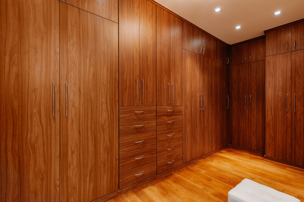 This is an example of an expansive modern gender-neutral dressing room in Los Angeles with flat-panel cabinets, medium wood cabinets and medium hardwood floors.