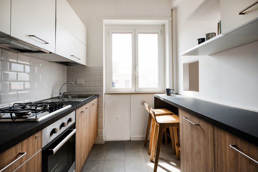 Design ideas for a mid-sized scandinavian galley separate kitchen in Rome with a drop-in sink, dark wood cabinets, laminate benchtops, white splashback, porcelain splashback, panelled appliances, porcelain floors, grey floor and black benchtop.