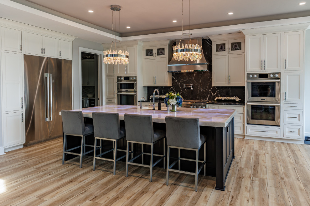 Inspiration for a large transitional l-shaped vinyl floor and brown floor open concept kitchen remodel in Milwaukee with an undermount sink, recessed-panel cabinets, white cabinets, quartzite countertops, black backsplash, stone slab backsplash, stainless steel appliances, an island and white countertops