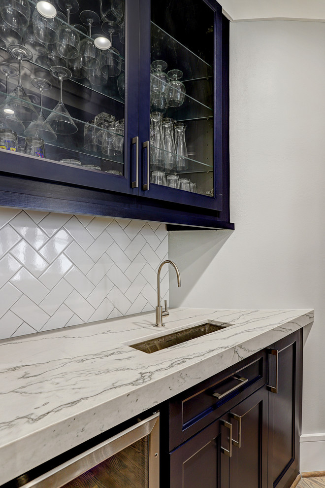 Inspiration for a mid-sized transitional galley light wood floor and beige floor wet bar remodel in Houston with a drop-in sink, glass-front cabinets, blue cabinets, quartzite countertops, white backsplash, subway tile backsplash and white countertops